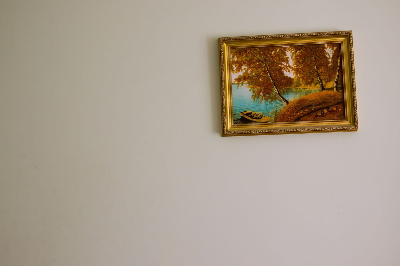 A gilt-framed painting of birch trees by a lake, hanging slightly crooked on a bare wall