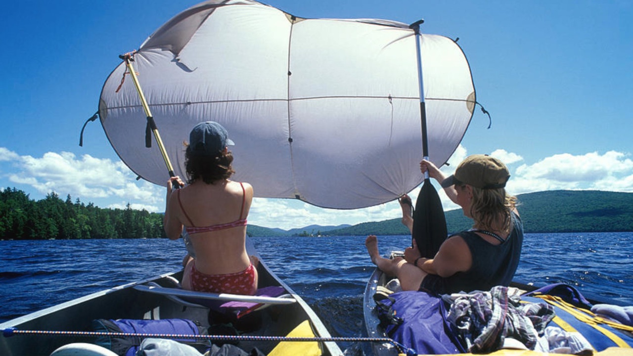 Two women in canoes on a lake hold up a tent as a makeshift sail