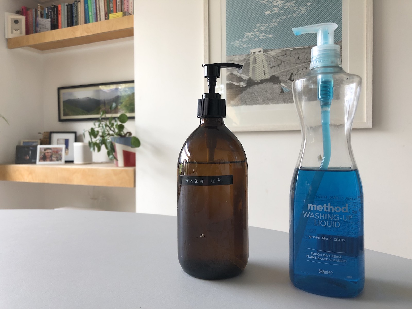 An amber glass pump bottle labelled Wash Up stands on a table beside a plastic bottle of Method washing-up liquid