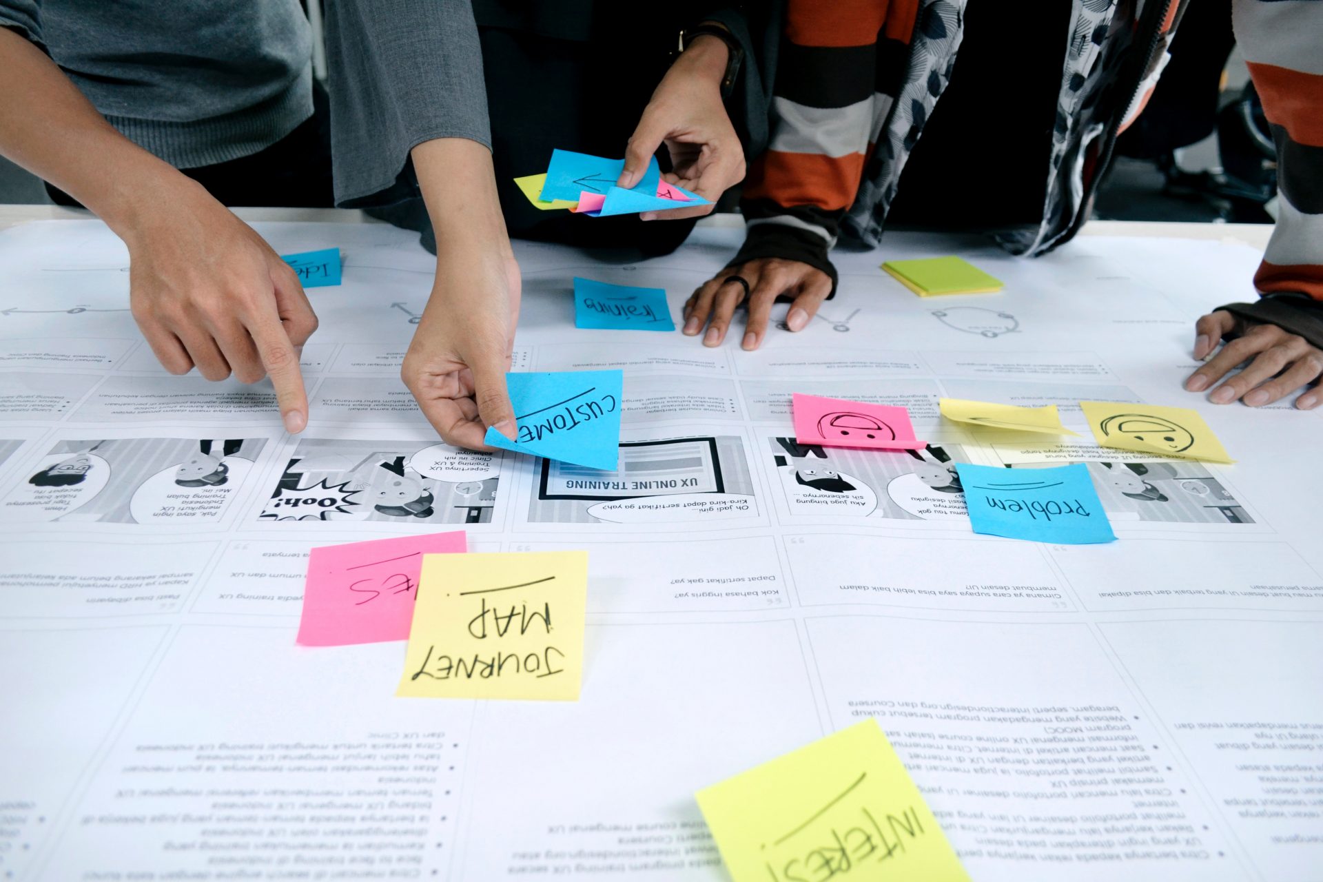 Hands moving sticky notes across a printed journey map during a workshop.